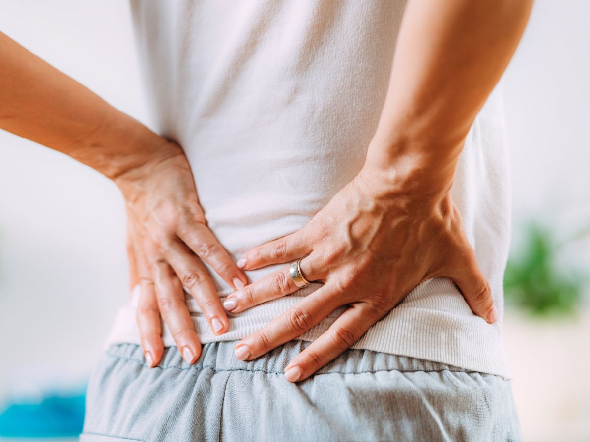 Eine Person die sich mit den Händen an den Rücken fasst