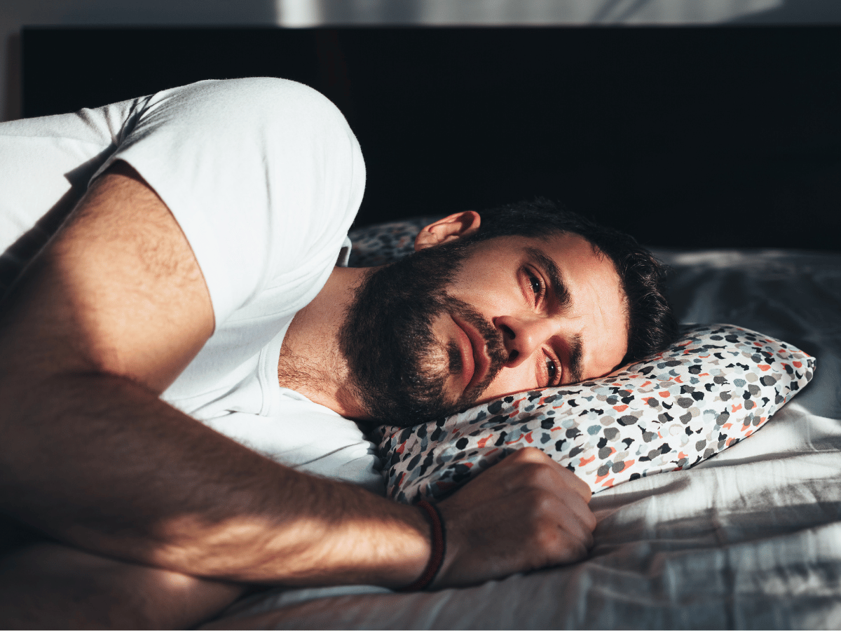 Ein Mann liegt im Bett mit traurigen Gesichtsausdruck 