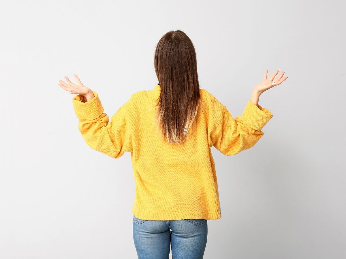 Eine Frau steht mit dem Gesicht zur Wand und trägt ein gelbes Oberteil 