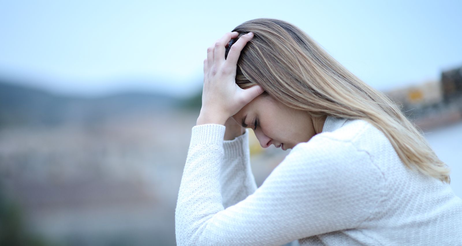 Eine Frau sitzt draußen und macht ihre Hände auf den Kopf 