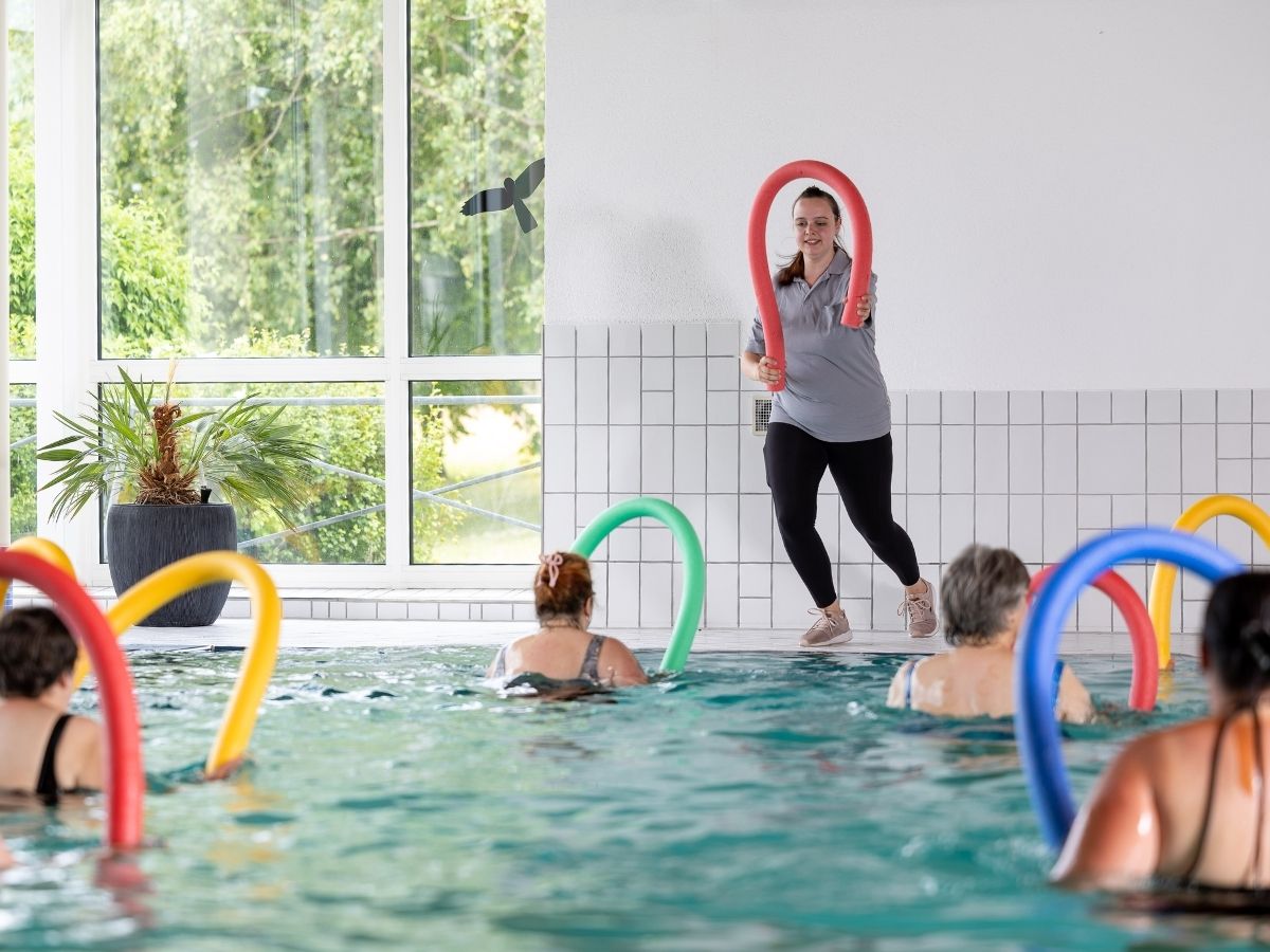 Eine Gruppe die im Wasser mit Schwimmnudeln Sport macht 