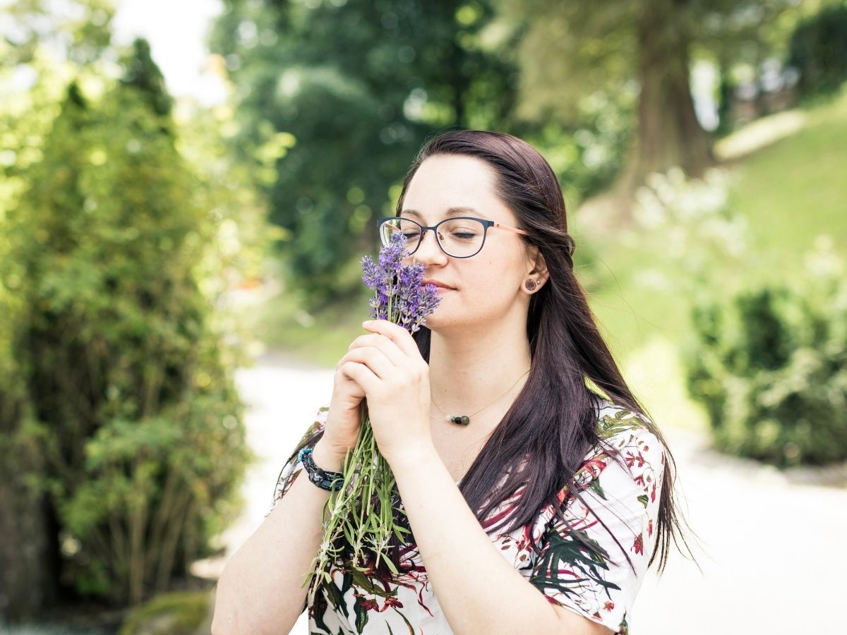 Eine Frauen die draußen an einer Blume riecht