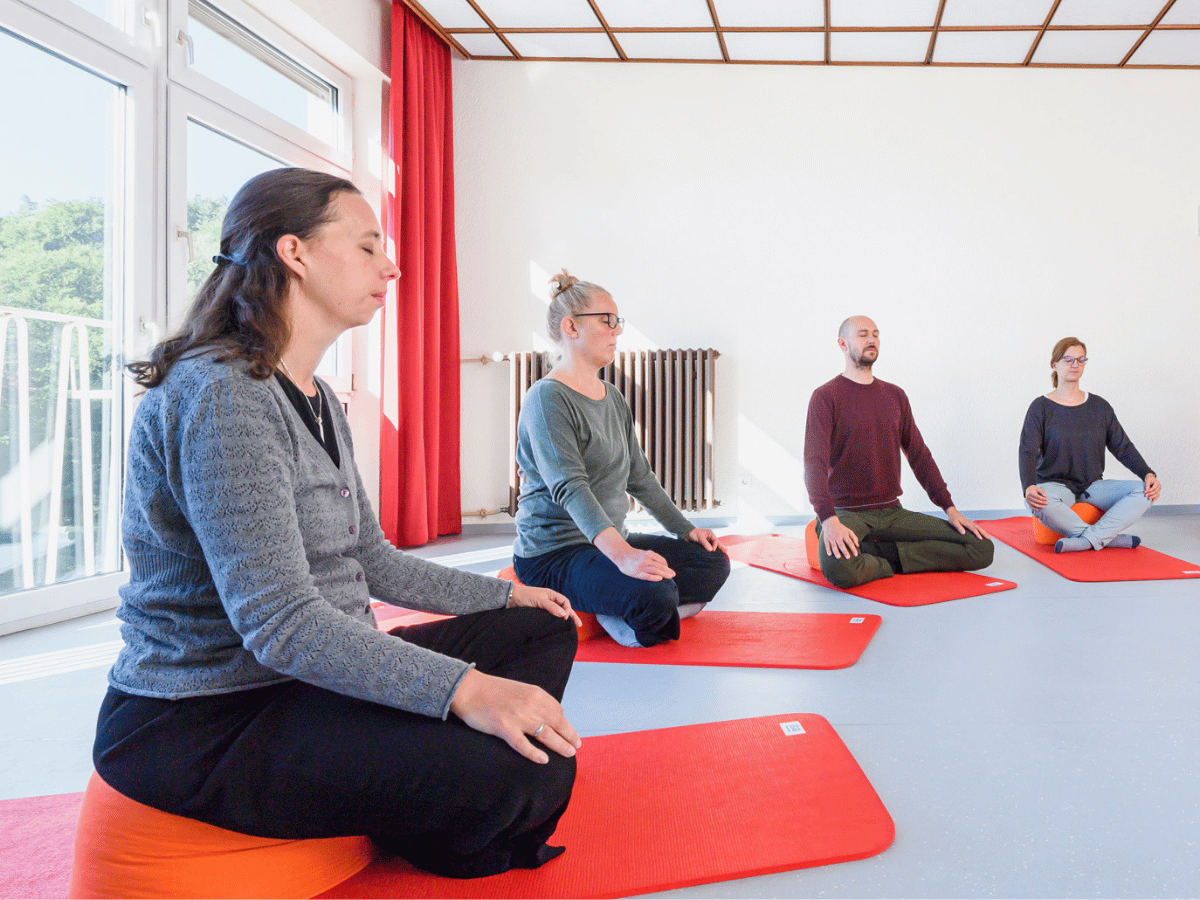Vier Personen sitzen auf roten Matten und trainieren 