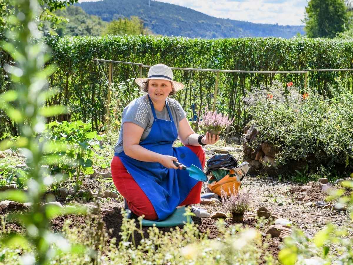 Die Frau sitzt im Beet und macht Gartenarbeit 