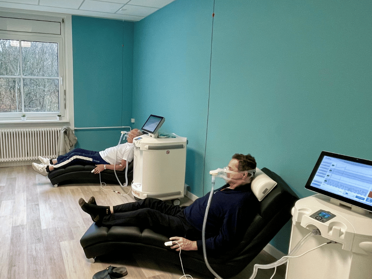 Die zwei Personen sitzen und sind an Inhalatoren 