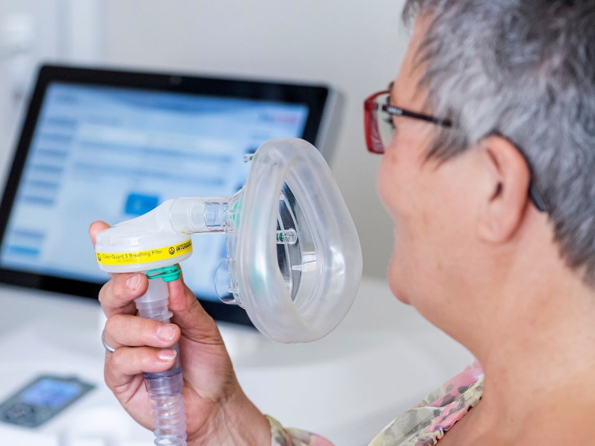 Die Frau hat ein Beatmungsgerät in der Hand und macht eine Inhalationsbehandlung im Rahmen der Inhalationstherapie