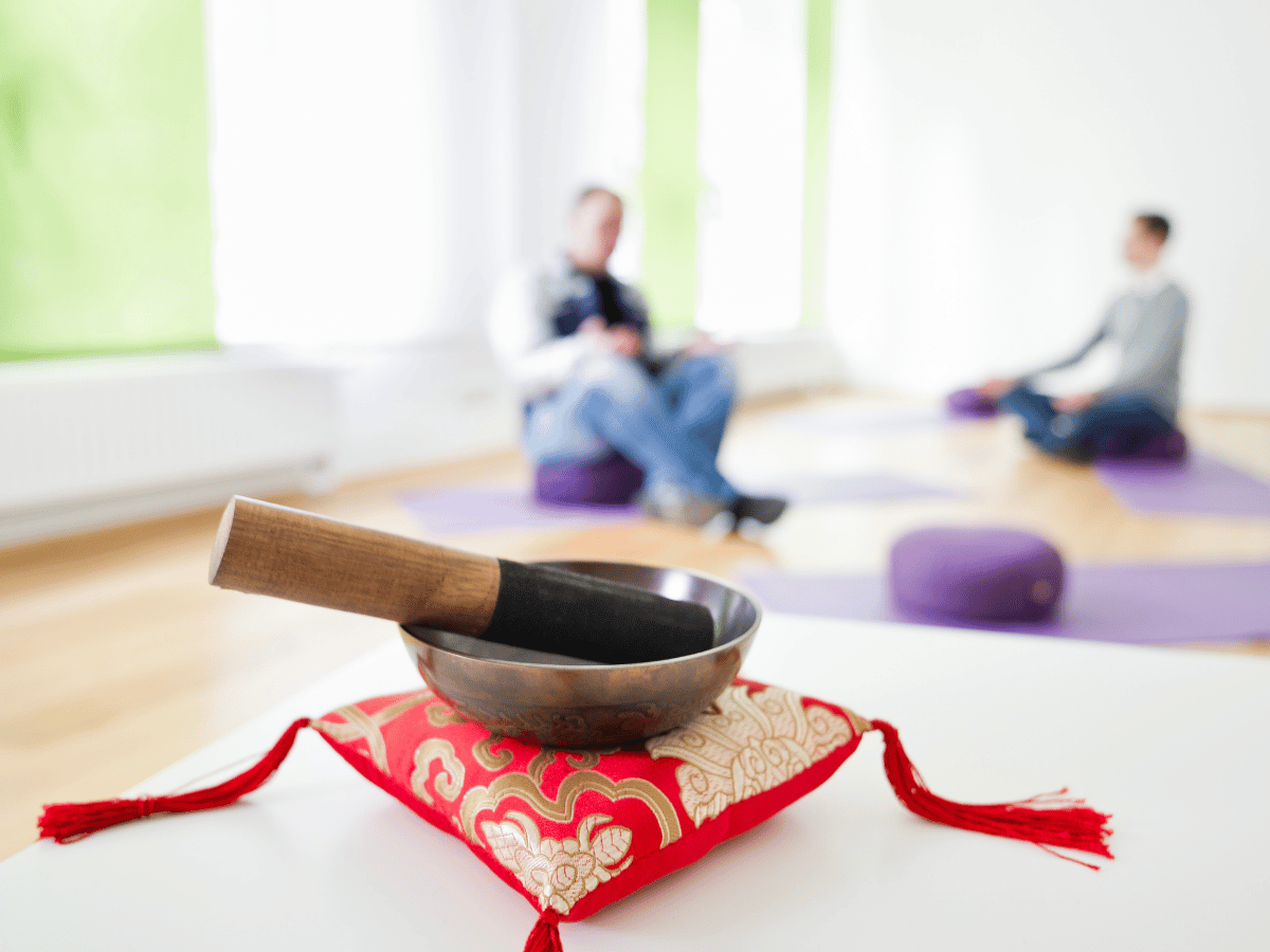 Eine Klangschale mit dem Stab auf einem roten Kissen 