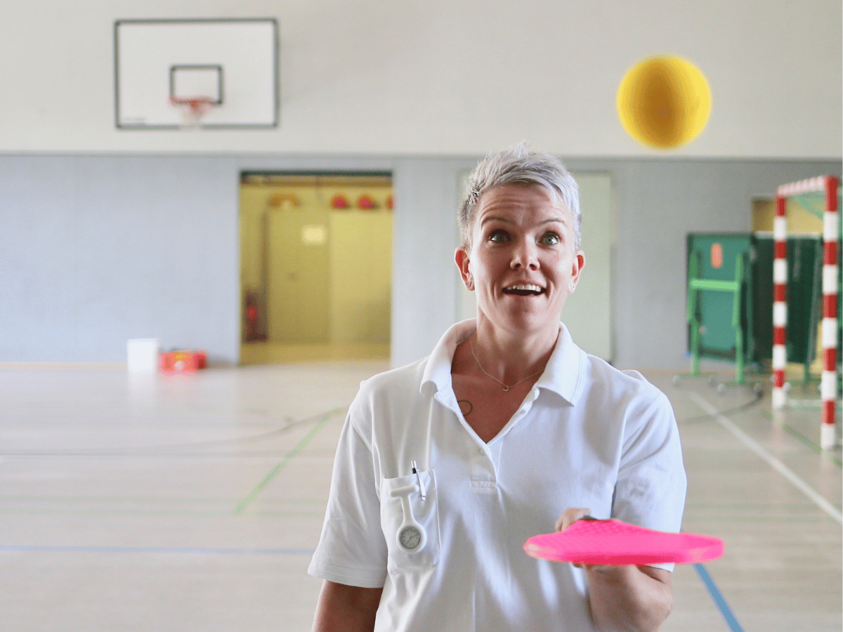 Die Frau versucht mit einem pinken Gegenstand den gelben Ball zu fangen 