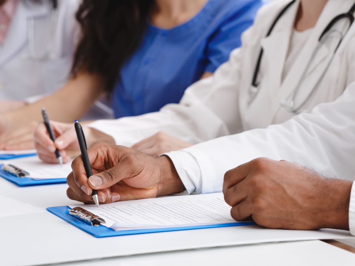 Menschen die auf Dokumenten schreiben, die auf Klemmbrettern liegen