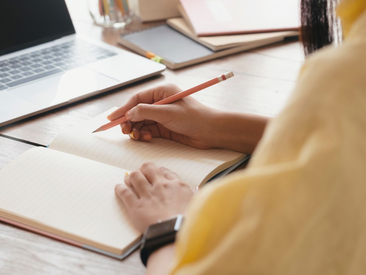 Eine Frau sitzt vor ihrem Computer und schreibt in ihr Notizbuch