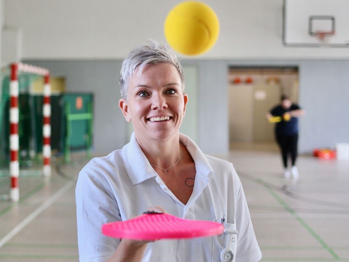 Die Frau versucht mit einem pinken Gegenstand den gelben Ball zu fangen 