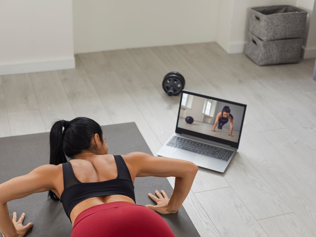 Eine Frau die die Übungen nachmacht die auf Ihrem MacBook zusehen sind 