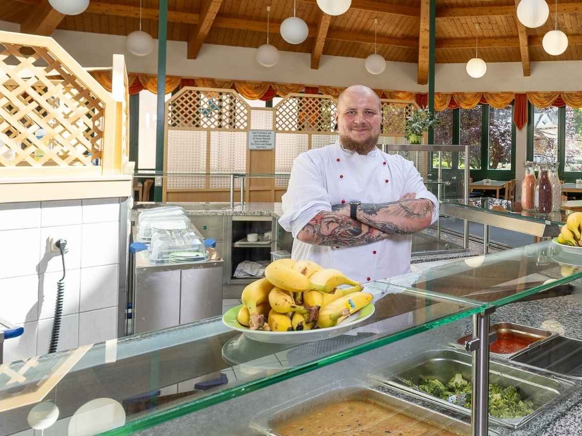 Ein Koch der vor dem Buffet steht und lächelt 