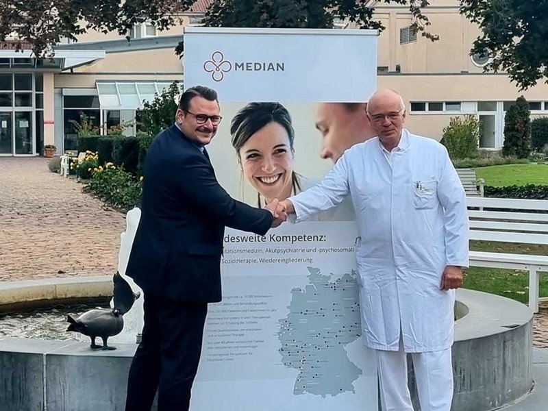 Zwei Männer die sich vor einem MEDIAN Aufsteller die Hand geben 