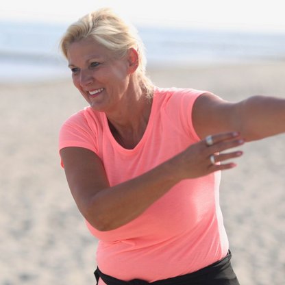 Frau im orangefarbenen Shirt macht am Strand Bewegungsübungen
