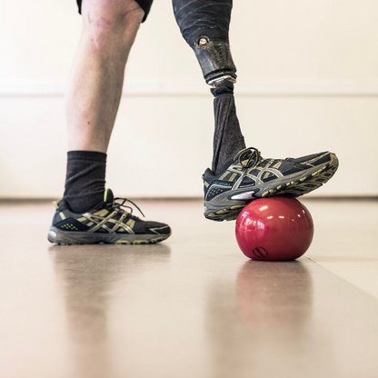 Eine Person die eine Prothese trägt und mit dieser auf einen roten Ball steht 