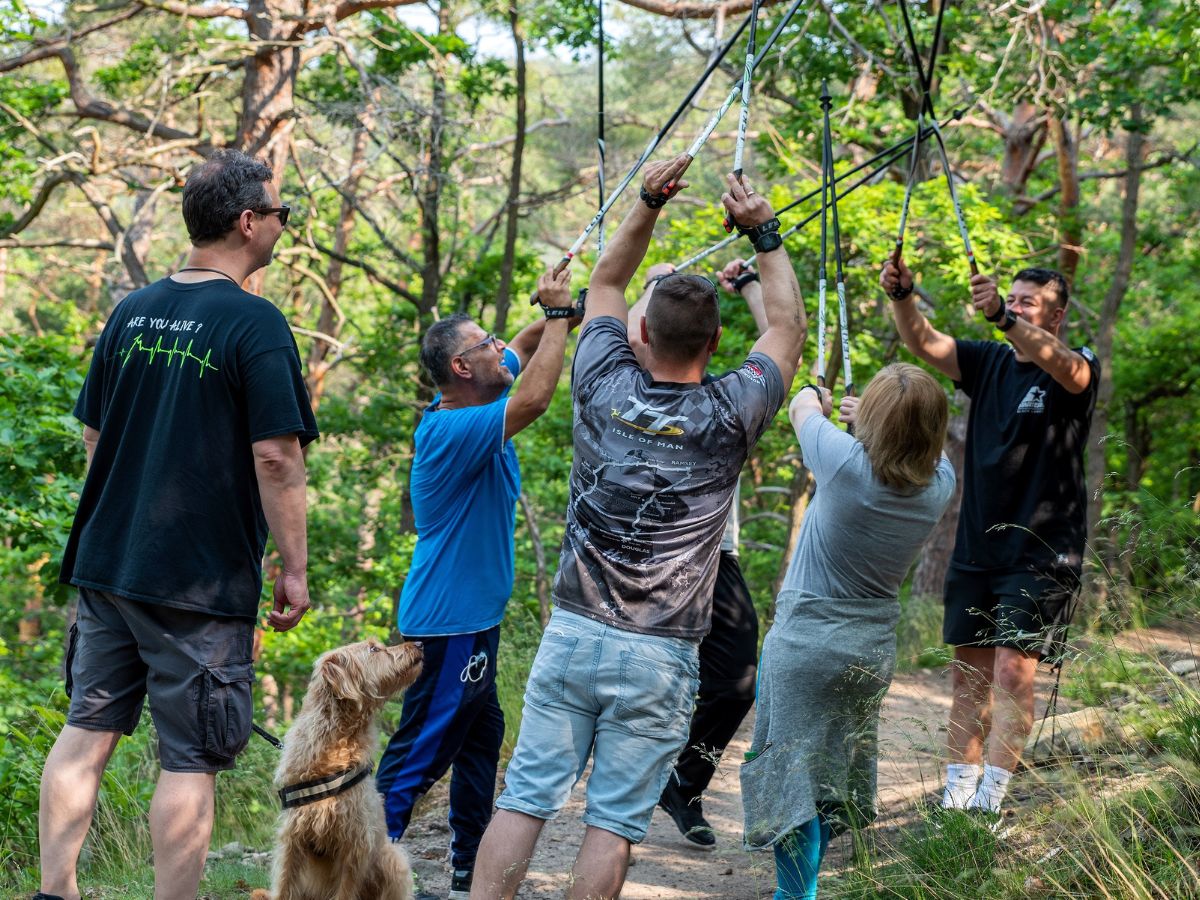 Personen sind im Wald, haben Wanderstöcke in den Händen und heben die Arme nach oben