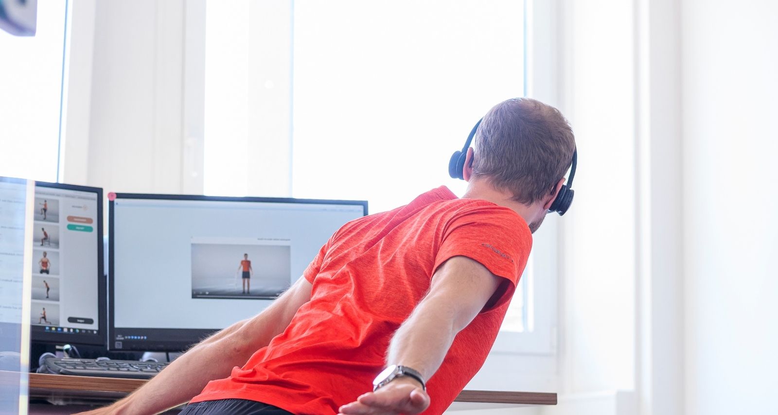 Mann macht in Bauchlage auf dem Stuhl Rückenübungen und schaut auf die Anleitung am Monitor