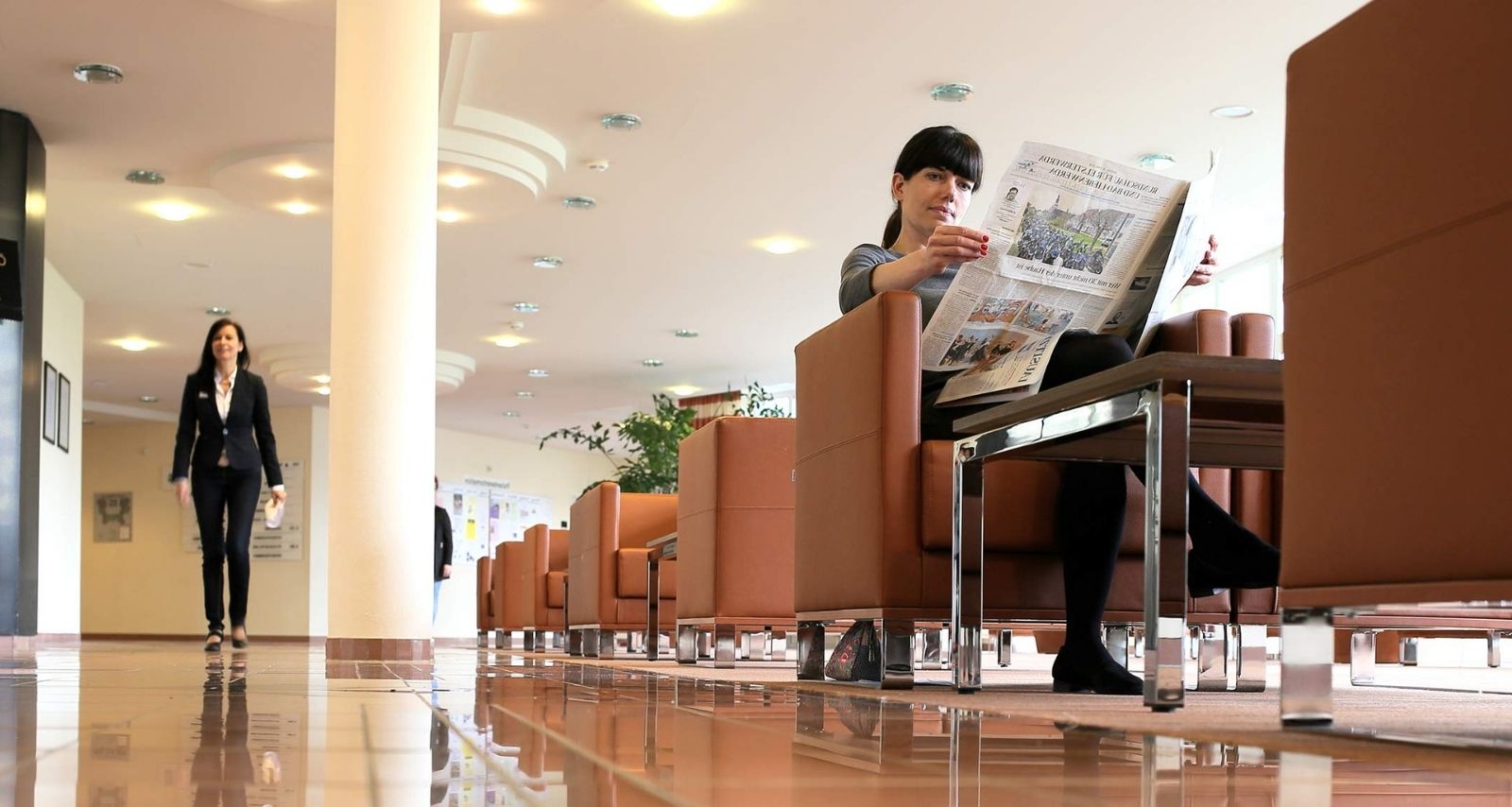 Patientin sitzt auf Couch im Foyer und liest eine Zeitung