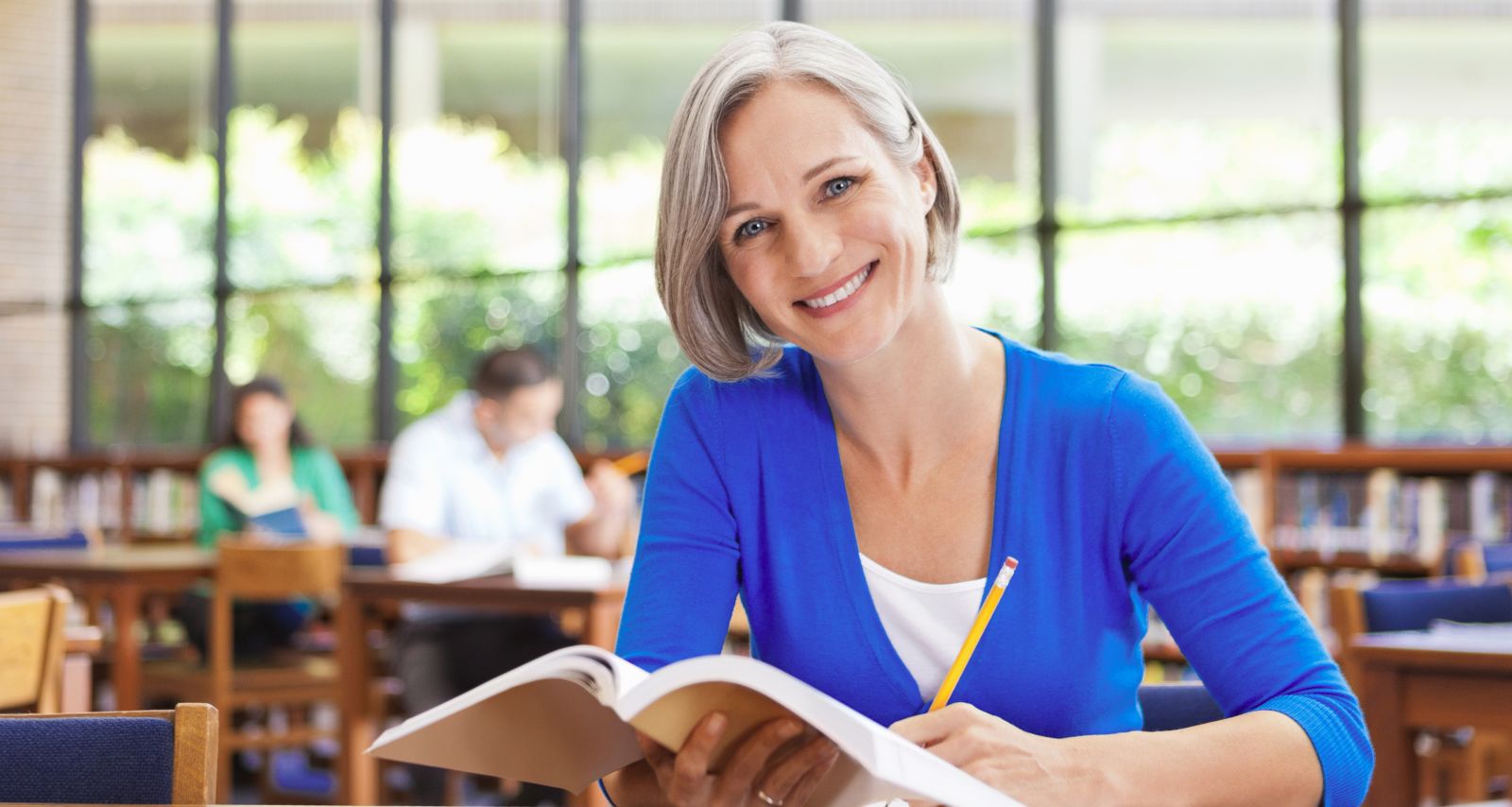 Eine Frau mit blauem Oberteil und Buch in der Hand, lächelt 