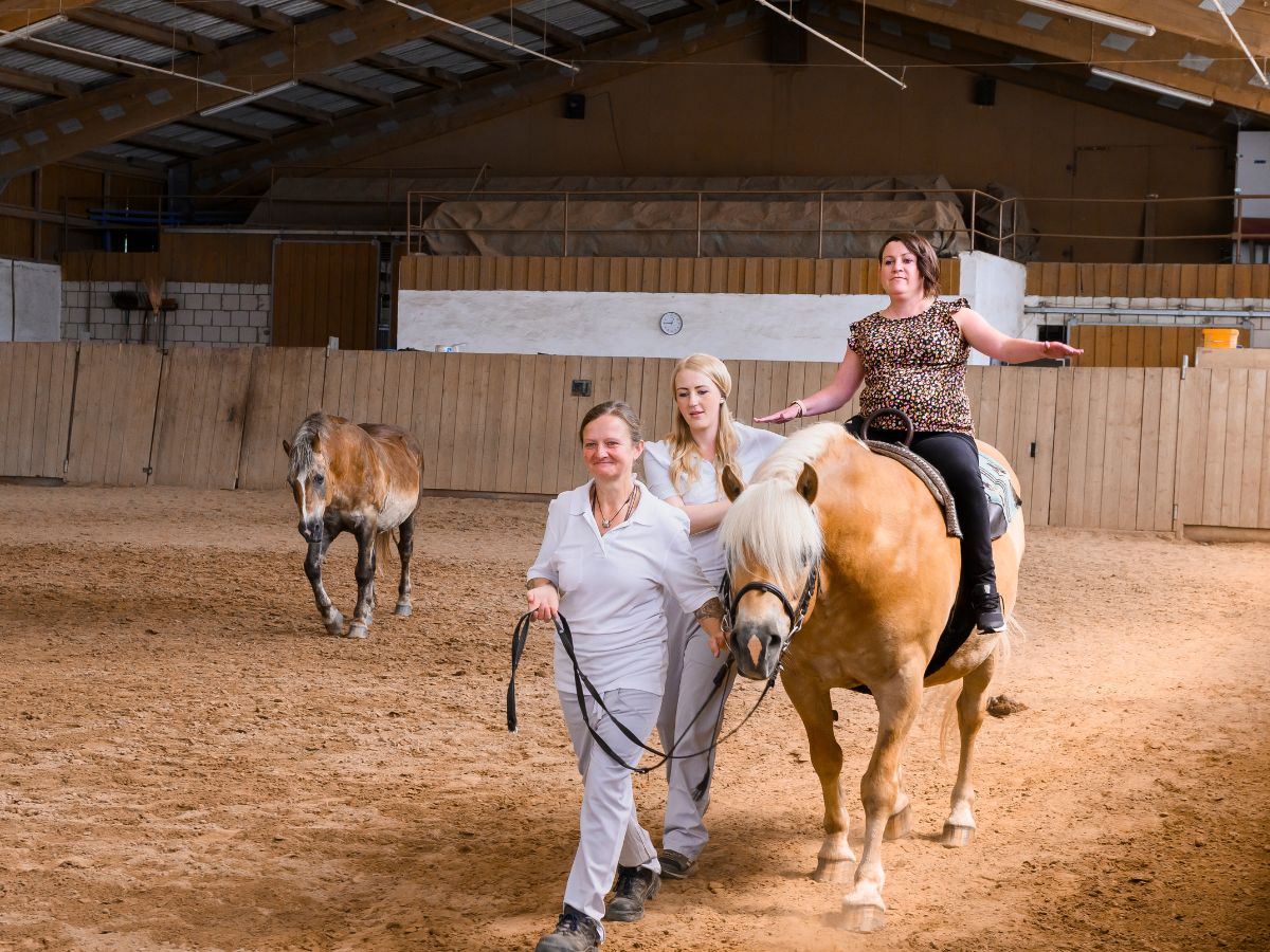 Patientin auf dem Pferd in Bergleitung von Therapeuten