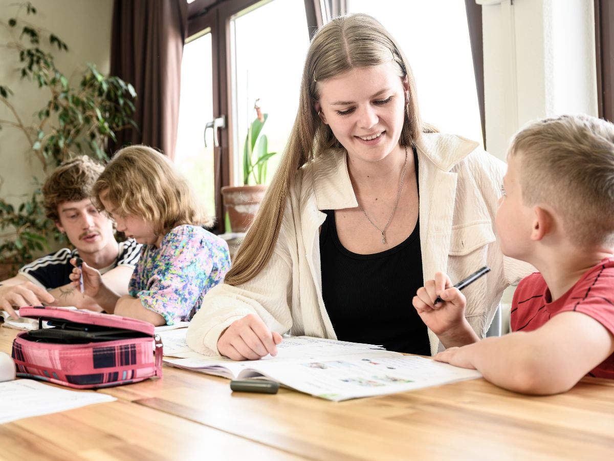 Eine Frau sitzt mit dem Jungen am Tisch und hilft ihm beim Schreiben
