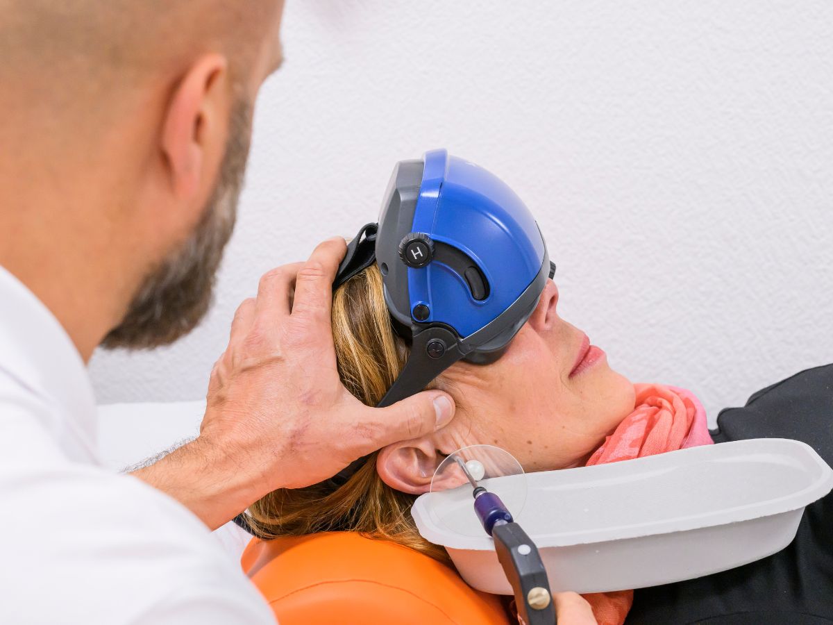 Patientin liegt mit einer Auffangschale am Ohr und Arzt spült das Ohr