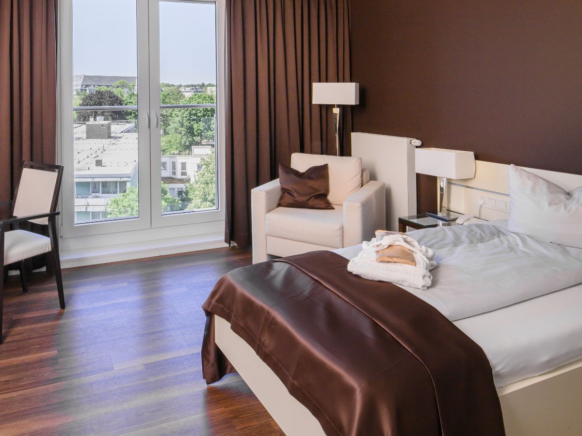 Komfort Zimmer mit Einzelbett, Sessel, Schreibtsich und Stuhl sowie Fernseher