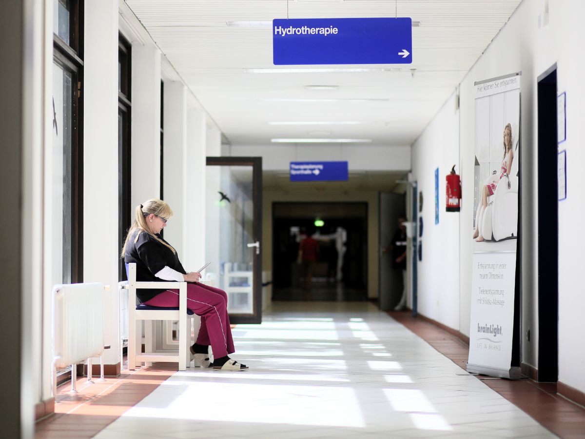 Klinikgang, am Rand sitzt eine Frau auf einer Bank