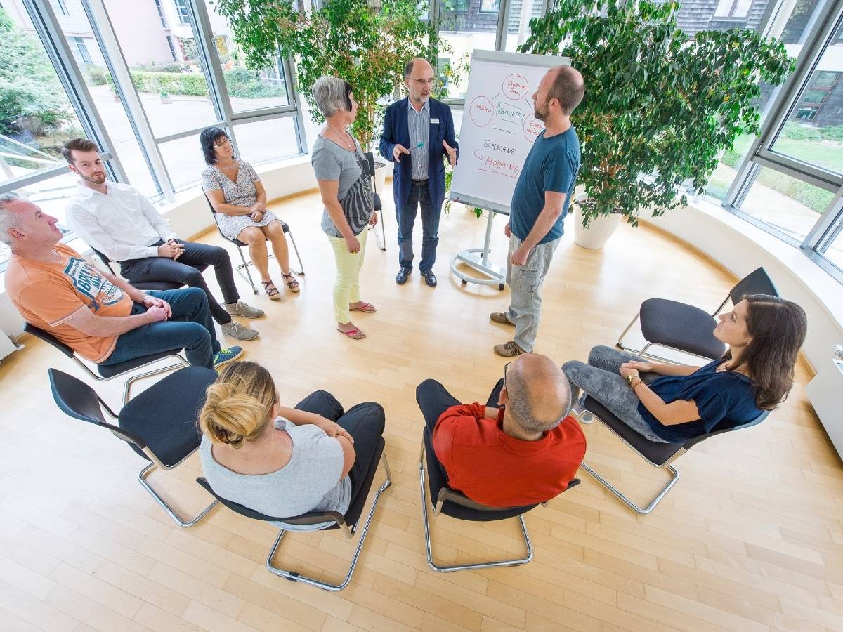 Personen sitzen im Stuhlkreis und schauen nach vorne 
