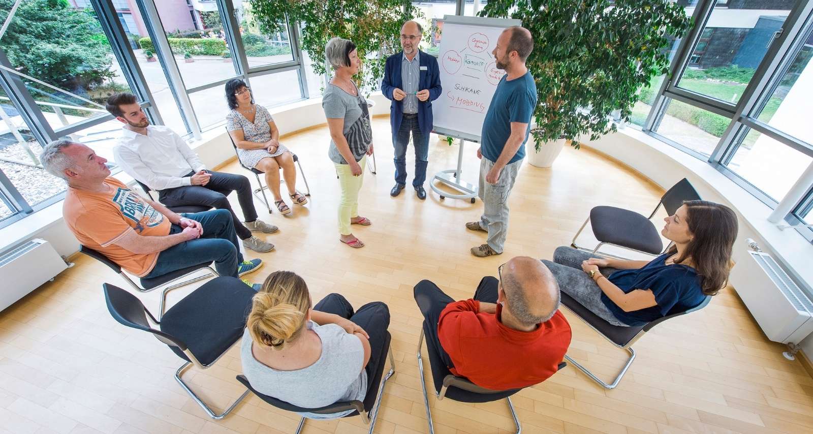 Personen sitzen im Stuhlkreis und schauen nach vorne 