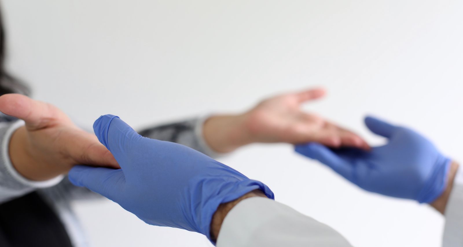 Eine Person mit blauen Handschuhen fasst die Hände einer anderen Person an 