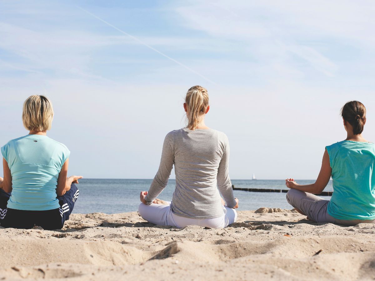 Drei Frauen sitzen im Schneidersitz am Strand und meditieren 