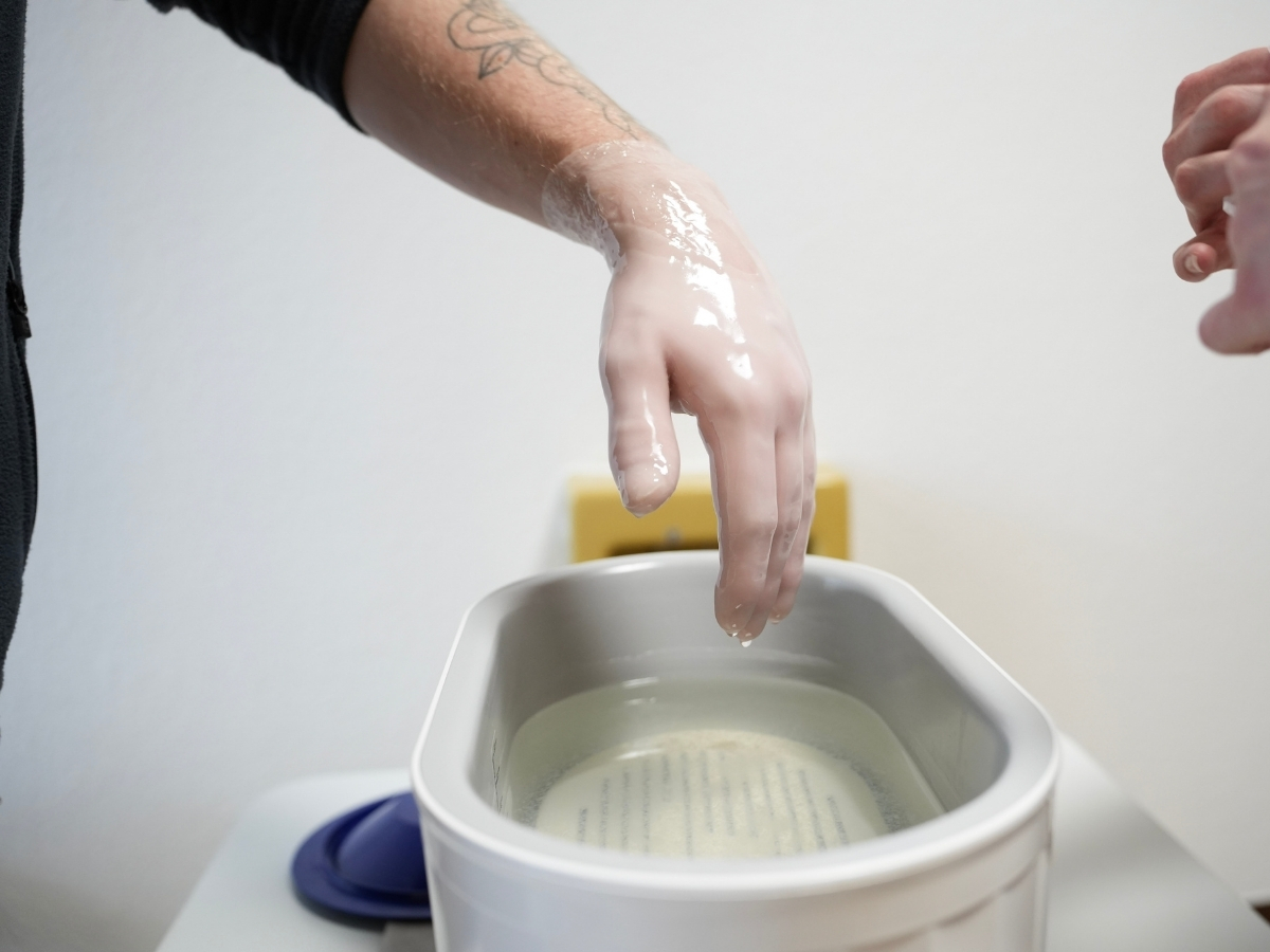 Mit Paraffin überzogene Hand über einem Wärmebad bei einer thermischen Anwendung