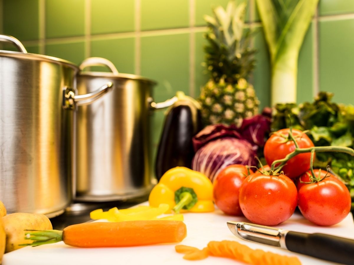 Töpfe auf Küchenplatte, daneben Paprika, Karotten und Tomaten