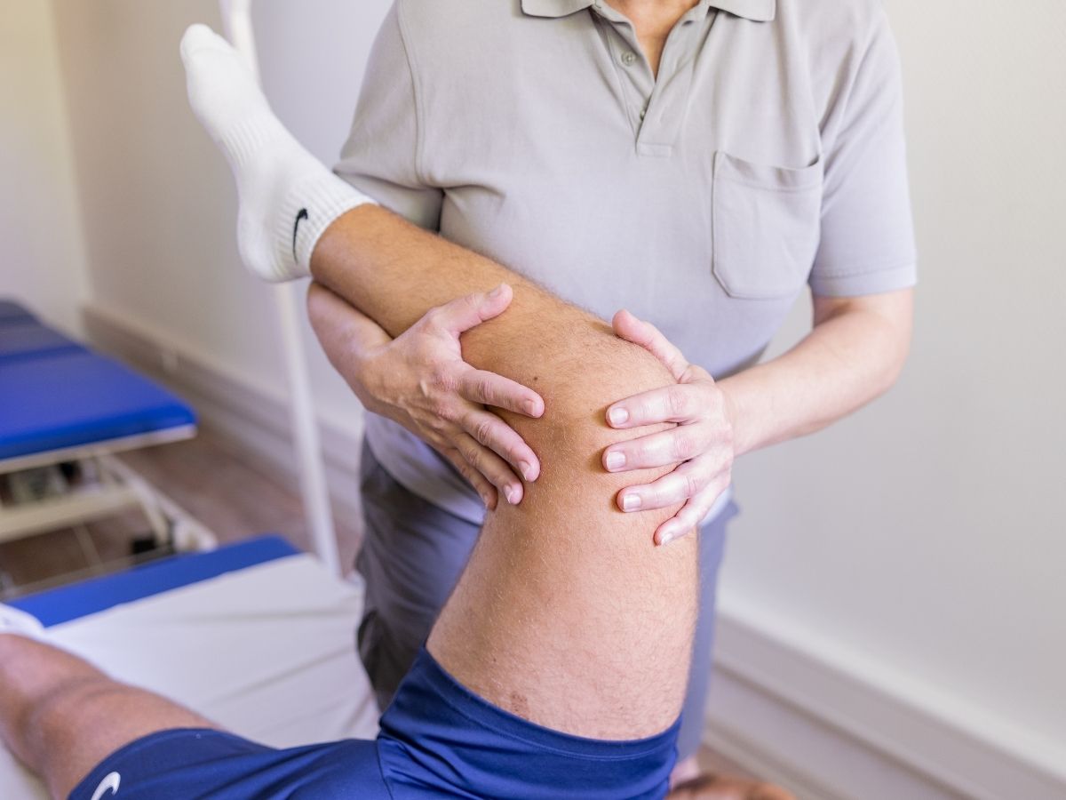 Therapeutin führt eine Physiotherapie am Knie eines Patienten durch