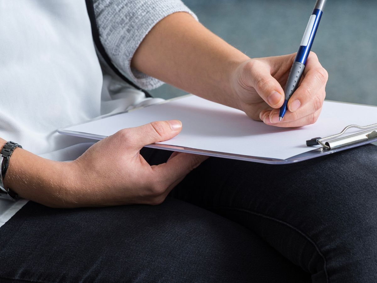 Eine Person schreibt auf einem Klemmbrett an dem ein Dokument dran ist 