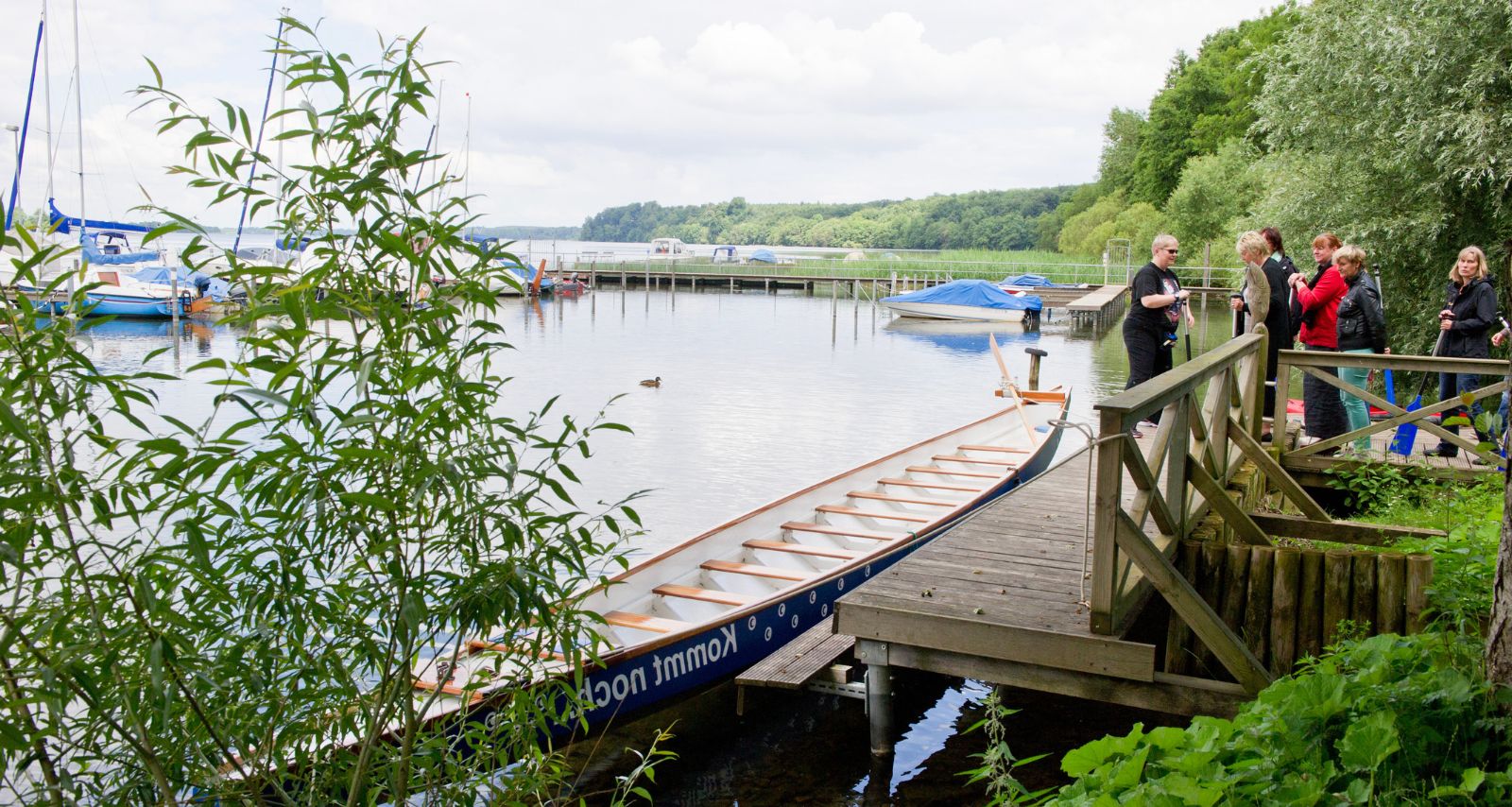Eine Gruppe steht auf einem Steg, vor einem Kanu 