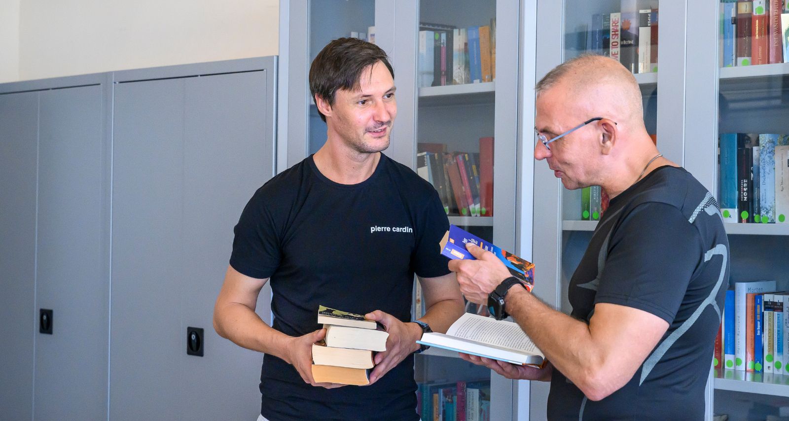 Zwei Männer stehen vor einem Buchregal und informieren sich über die Bücher.