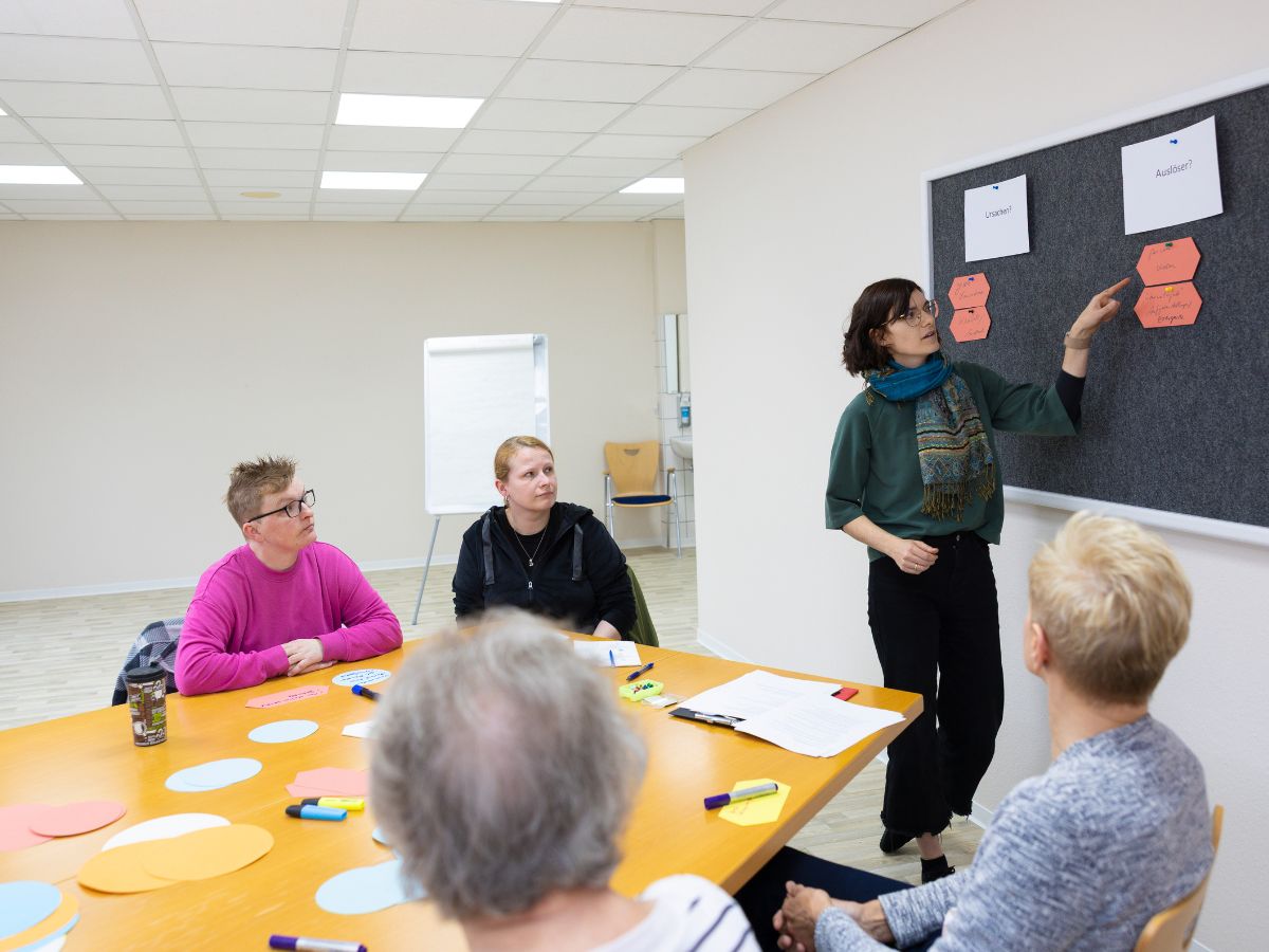 Eine Frau, die an der Tafel steht, erklärt der Gruppe etwas