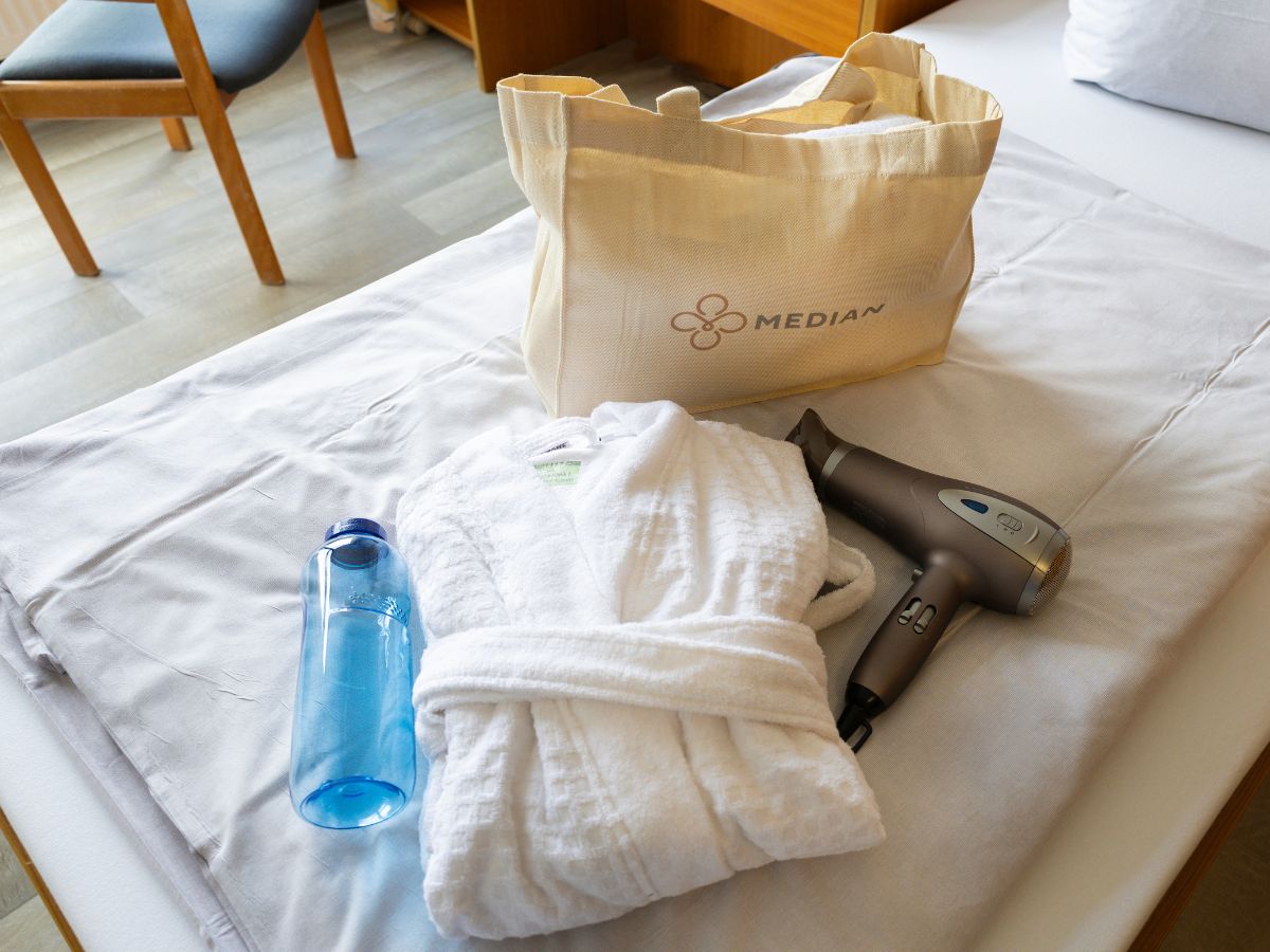 Flasche, Föhn, Bademantel und Tasche liegen auf dem Bett