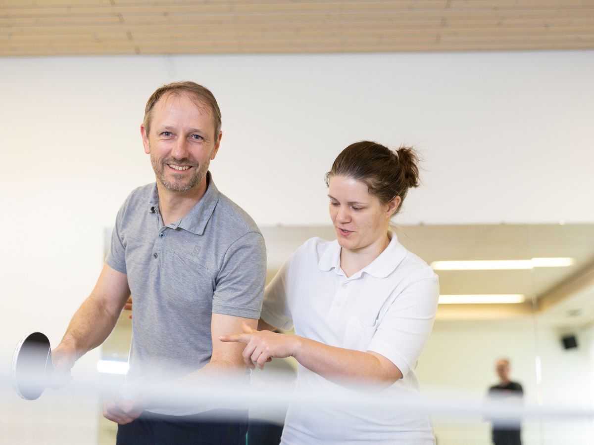 Eine Therapeutin begleitet den Mann, der Tischtennis spielt