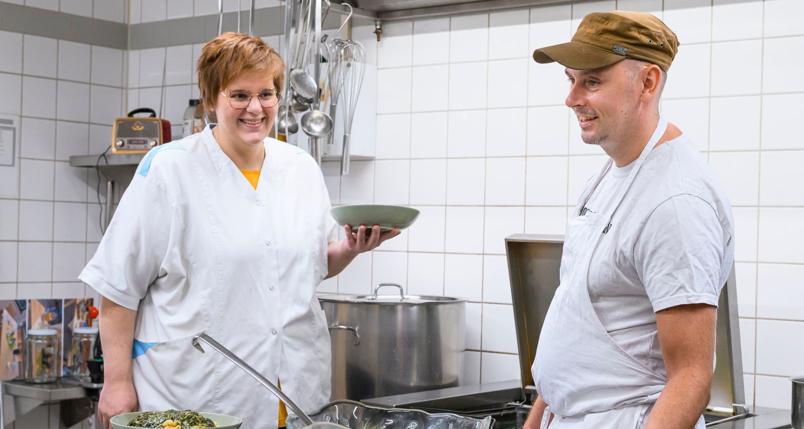 Eine Frau und ein Mann bereiten in einer Großküche Mahlzeiten vor.