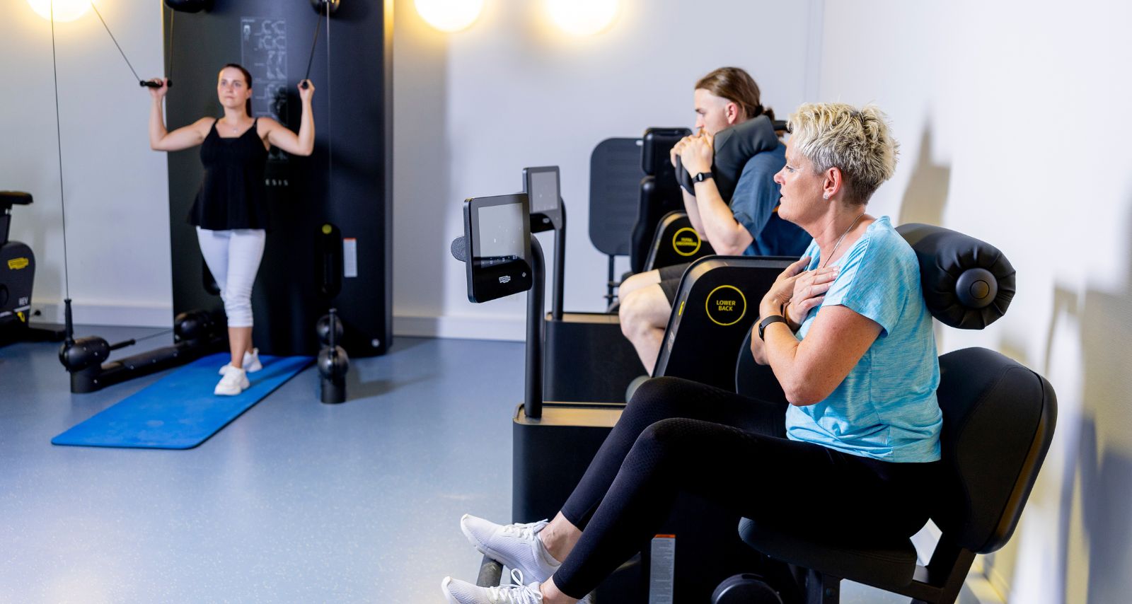 Drei Personen die an unterschiedlichen Geräten Übungen durchführen 