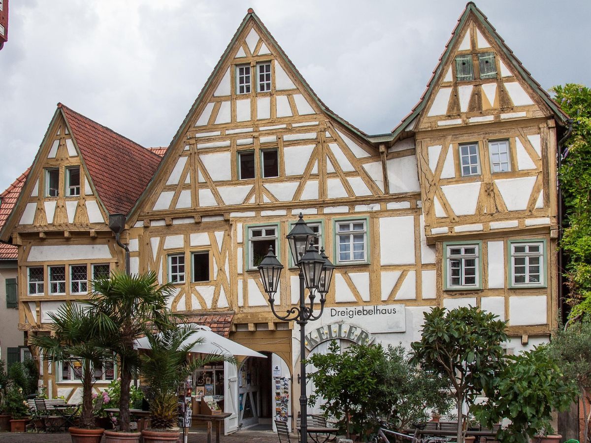 Drei helle Fachwerkhäuser mit spitzen Giebeln in Besigheim, davor Pflanzen und Außensitzplätze