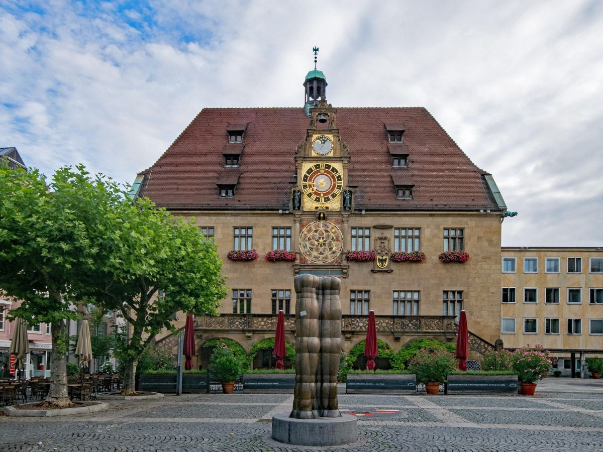 Heilbronner Rathaus mit großer Uhr am Giebel, davor ein Brunnen und seitlich Bäume
