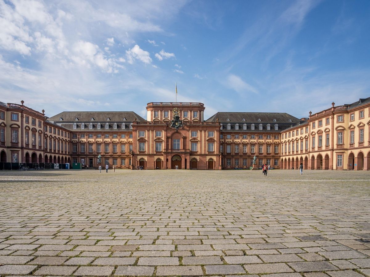 Symmetrische Schlossfassade in Mannheim mit Seitenflügeln hinter einem weitläufigen gepflasterten Ehrenhof