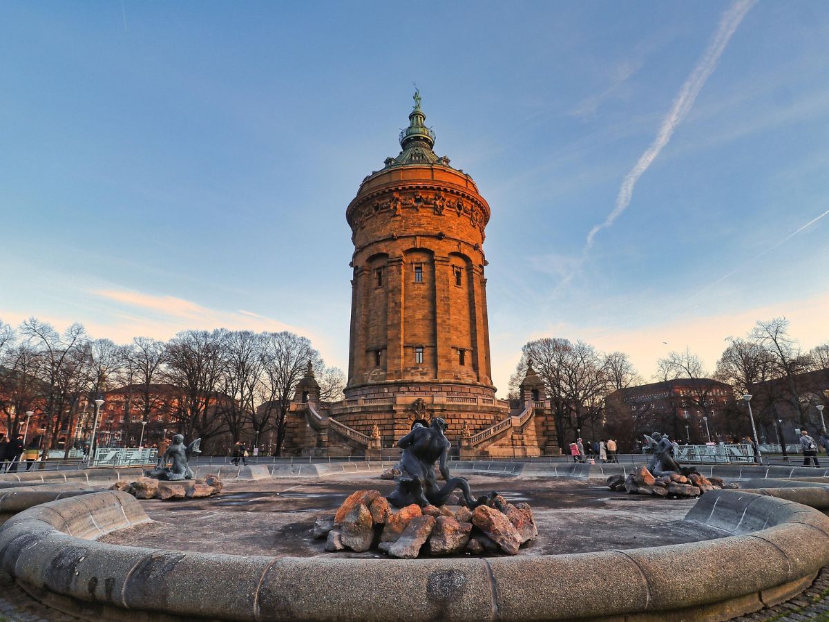Sandsteinfarbener Mannheimer Wasserturm hinter einem runden Brunnenbecken mit Figuren