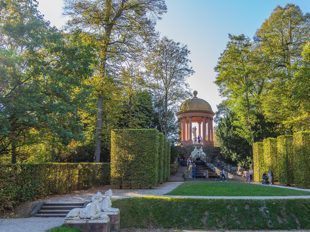 Runder Apollotempel auf einem Felsaufbau am Ende einer von Hecken gesäumten Allee in Schwetzingen