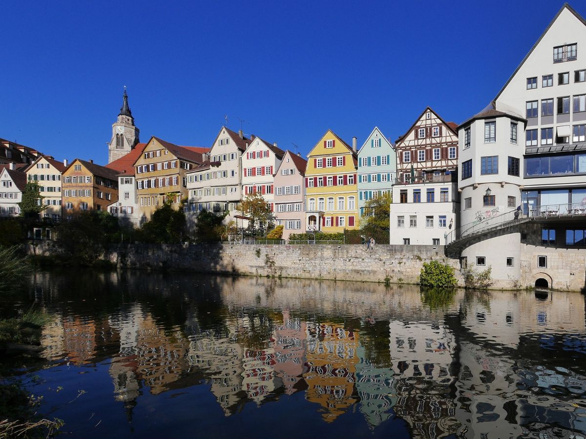 Bunte Giebelhäuser am Neckar in Tübingen mit Spiegelung im Wasser und einer Kirche im Hintergrund